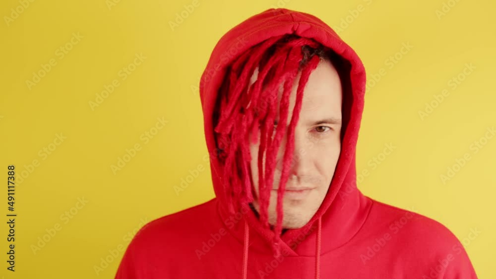 Young man with red dreadlocks in hood nodding head with disagreement. Smiling male showing gesture of disagreement and closing eyes.