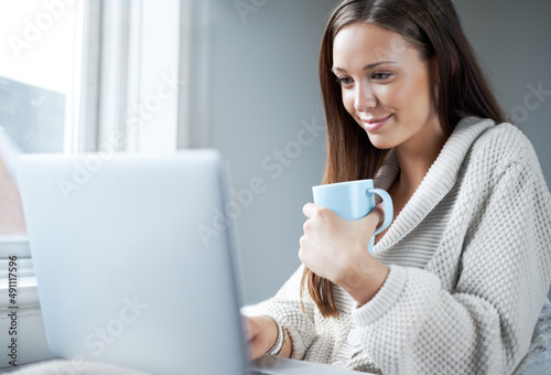 Ive got mail.... Attractive young brunette sipping coffee while sitting at home in front of her laptop.