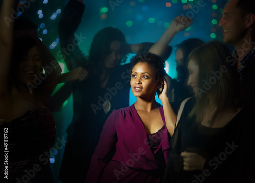 She stands out on the dance floor. Shot of a smiling young woman standing on a dance floor in a nightclub surrounded by people.