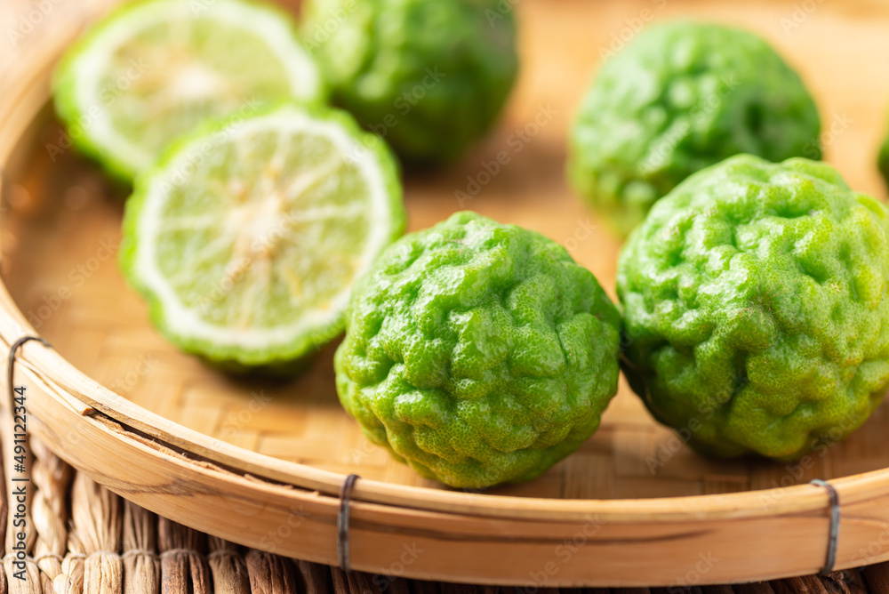 Organic Kaffir lime in bamboo basket, Citrus fruit used in Southeast Asian cuisine and essential oil Organic Kaffir lime in bamboo basket, Citrus fruit used in Southeast Asian cuisine and essential oil
