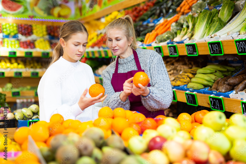 Female grocery store clerk helps teenage girl pick ripe fruits
