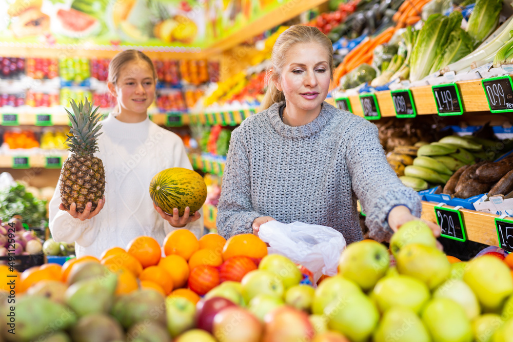 Mom and her teen daughter pick pineapple and melon at the grocery supermarket