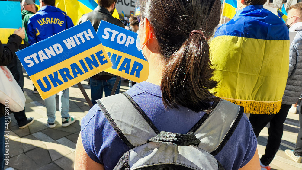 A girl with a backpack holds posters with the inscription stop the war and stand with Ukraine