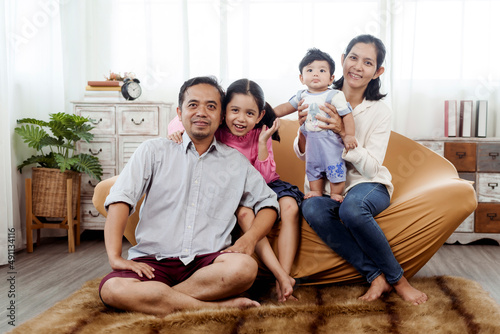 Love and warmth in Asian families, parents and children. Sitting on the sofas in the living room, with love and warmth from parents to the newborn baby and sister. © Ekkasit A Siam