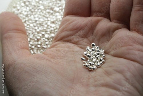 A white Caucasian person holds in hand grains of precious metal, precisely sterling silver which is important in stocks, jewelry and industrial use and gets expensive during crisis.