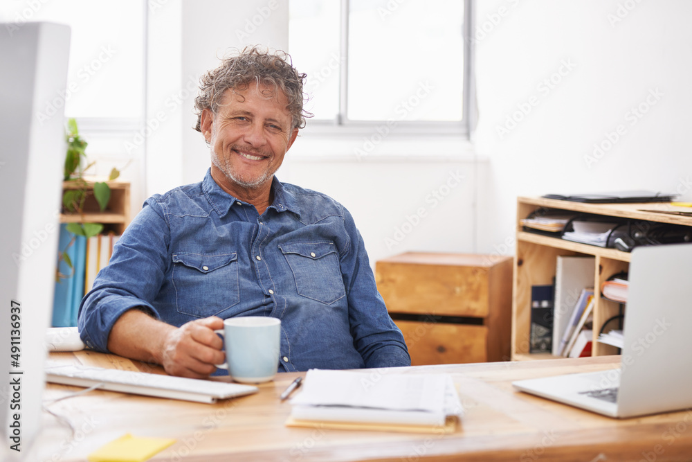 Hes a relaxed kind of boss. Portrait of a mature businessman having coffee while sitting at his desk.
