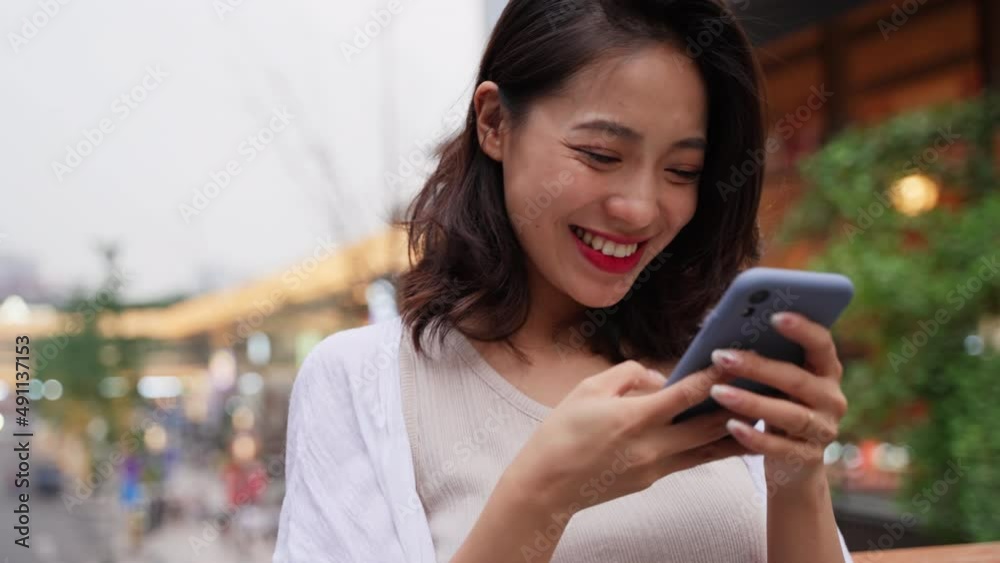 happy young asian woman looking at mobile phone in the city