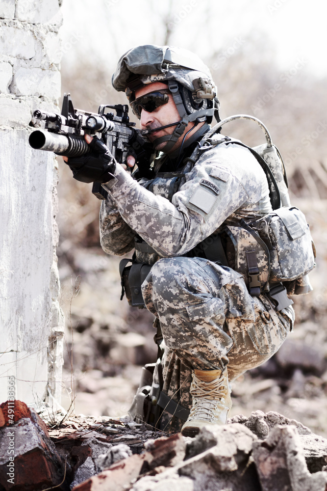 Leading the assult. A soldier crouched down next to a broken down wall and pointing his gun into the distance.