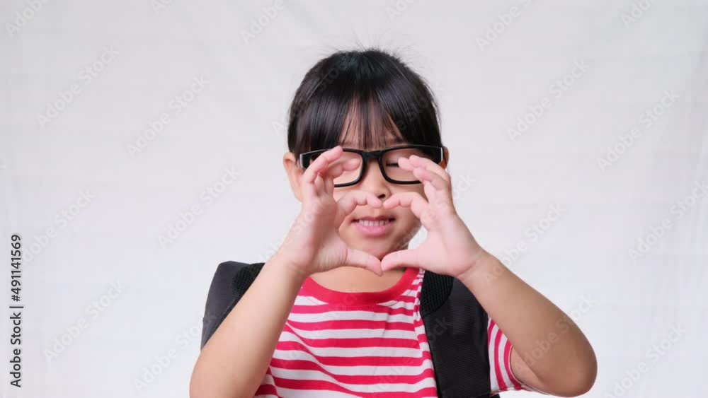 Happy schoolgirl wearing casual outfit with backpack and doing heart-shaped hands on white background in studio. Back to school concept Happy schoolgirl wearing casual outfit with backpack and doing heart-shaped hands on white background in studio. Back to school concept