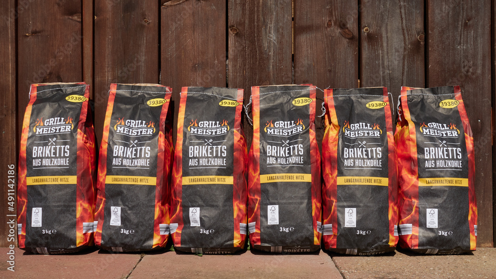 Grill Meister briquettes made of charcoal, house brand of the company Lidl,  sacks on a floor made of stone plates and a background made of wooden  boards, Germany. Stock Photo | Adobe