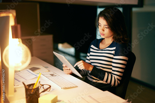 Shes as equally productive through the day and night. Shot of a young businesswoman working late on a digital tablet in an office.