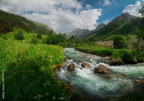 A high-mountain river with clear water flows in a picturesque mountain valley with bright greenery.