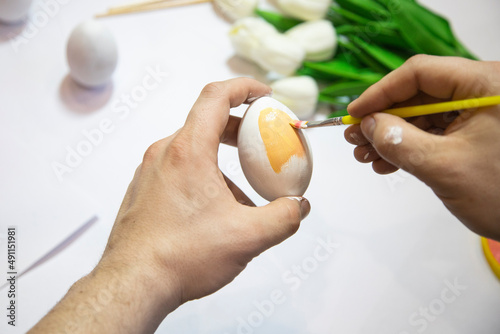 A man's hand paints an Easter egg with a yellow brush close-up. The concept of the holiday and Easter decor