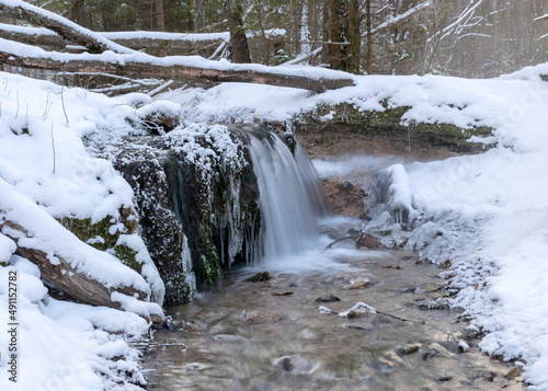 landscape with a small rapid river flowing over frozen rocks through a wild ravine