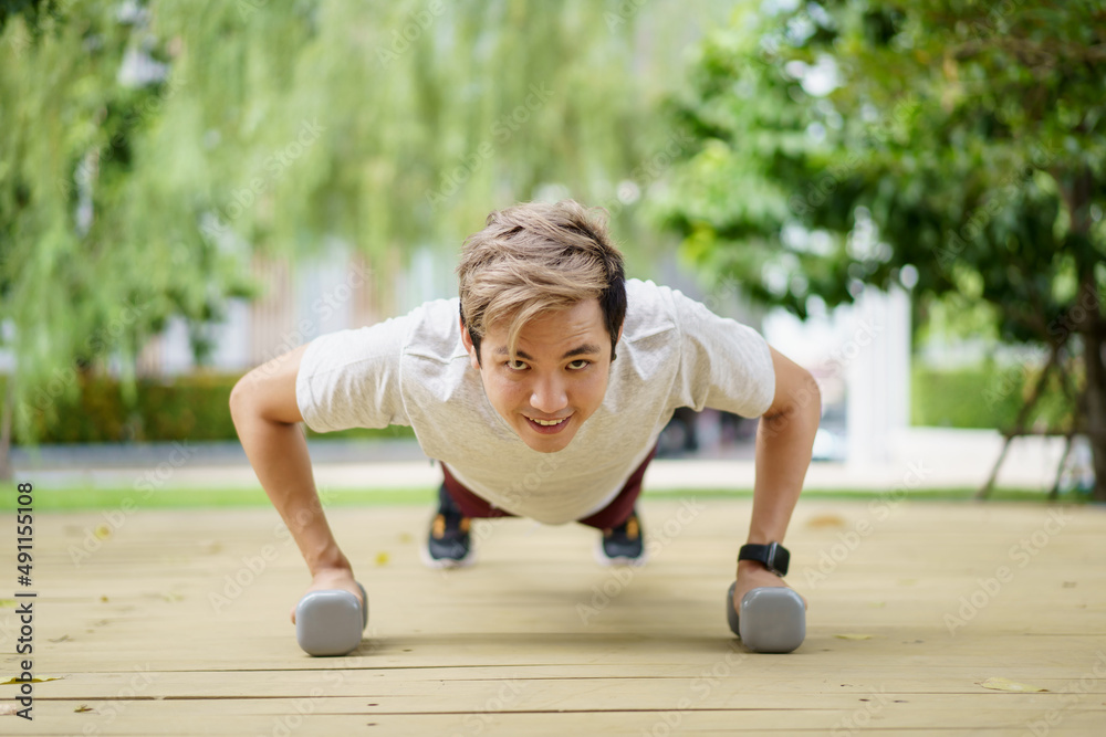 Naklejka premium Active Asian sportsman making a body weight exercise, man doing push up workout with dumbbell. 