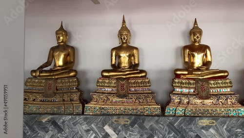 BANGKOK, THAILAND - Circa November, 2021: Golden buddha statues with bhumisparsa mudra gesture at Wat Pho, Temple of Reclining Buddha. Row of sitting buddha images on gilded pedestal  - tracking shot photo