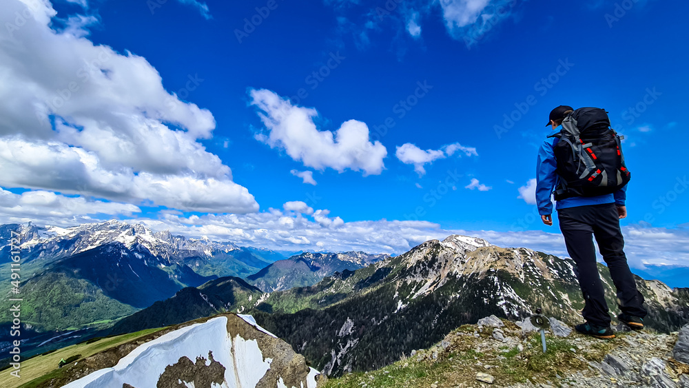 Hiker man with backpack at the summit of Frauenkogel (Dovska Baba) with scenic view on mountain peaks in the Karawanks and Julian Alps, Carinthia, Austria. Border with Slovenia. Triglav National Park