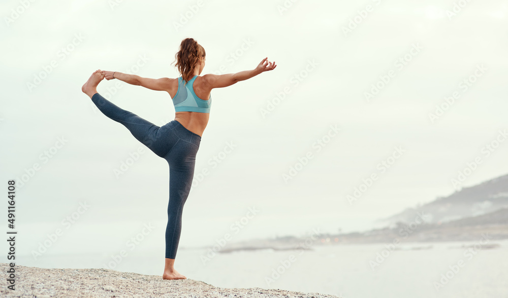 Balance is key in everything you do. Rearview shot of a sporty young woman practicing yoga at the beach.
