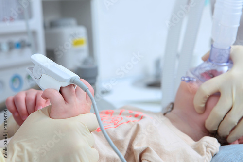 Child is under general anesthesia. Surgery under anesthesia. Operating room .Oxygen mask on the child's face.Measurement of oxygen levels in the blood. A child's hand.Face is out of focus.