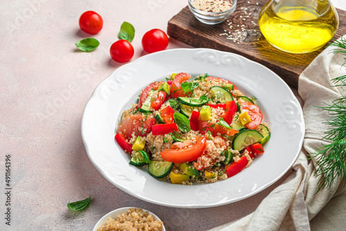 A portion of salad with quinoa, avocado, tomatoes and cucumber and red pepper on a light background.