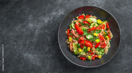 Fresh vegetable salad with avocado, tomatoes, cucumber and quinoa on a dark background.