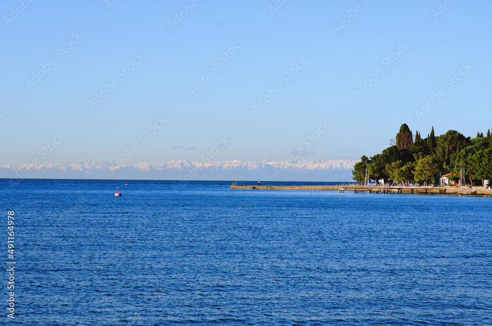 Wonderful view of the snow covered Alps mountains against blue Adriatic Sea and sky in winter holidays. Slovenia, Strunjan