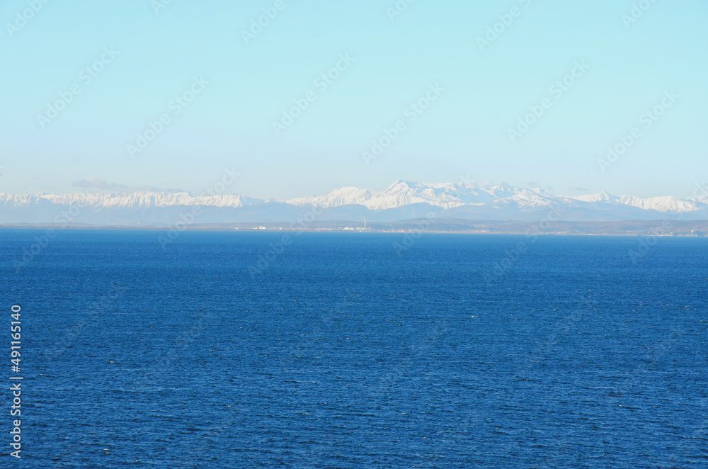 Wonderful view of the snow covered Alps mountains against blue Adriatic Sea and sky in winter holidays. Slovenia, Strunjan