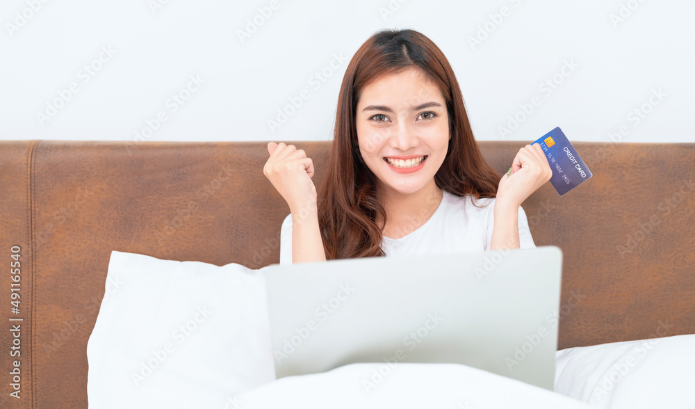 Happy asian woman doing online shopping at home, Women shopping online with credit card and laptop on the bed at home Happy asian woman doing online shopping at home, Women shopping online with credit card and laptop on the bed at home