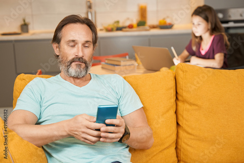 Adult man is using smartphone on sofa in living room