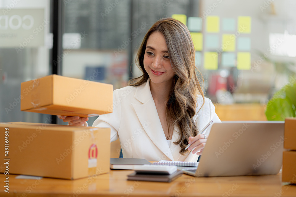 The owner of an online store is checking orders for packaged products in order to prepare them for delivery to customers as ordered through the website. Online selling and online shopping concepts. The owner of an online store is checking orders for packaged products in order to prepare them for delivery to customers as ordered through the website. Online selling and online shopping concepts.