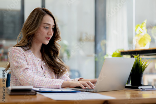 A beautiful Asian businesswoman sitting in her private office, she is checking company financial documents, she is a female executive of a startup company. Concept of financial management.