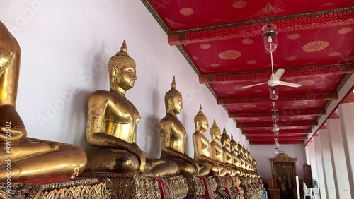 BANGKOK, THAILAND - Circa November, 2021: Golden buddha statues with bhumisparsa mudra gesture at Wat Pho, Temple of Reclining Buddha. Row of golden sitting buddha images on gilded pedestal photo