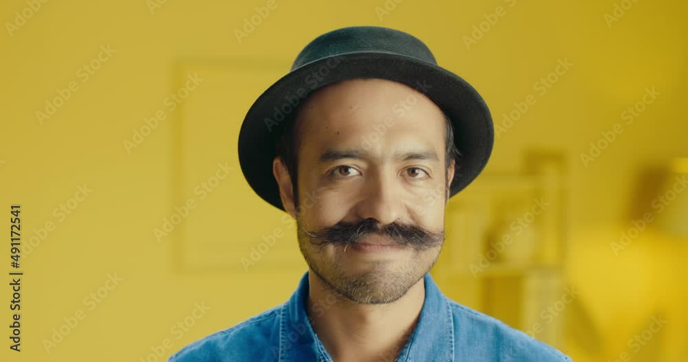 Happy confident Hispanic guy with mustache posing for headshot face front close up portrait in the studio with monochrome yellow background. Smiling handsome man with mustache looking at camera