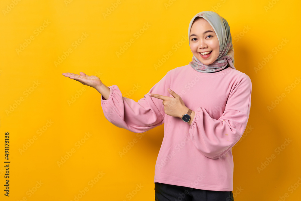 Smiling young Asian woman in pink shirt showing copy space on palm on yellow background