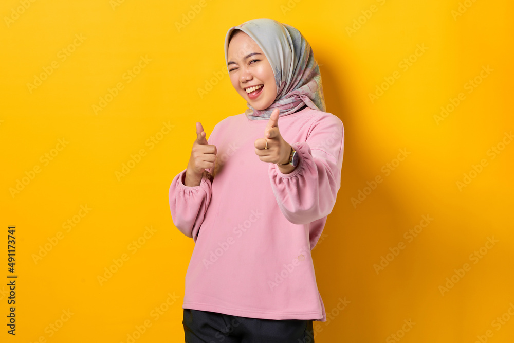 Cheerful young Asian woman in pink shirt pointing fingers at camera on yellow background Cheerful young Asian woman in pink shirt pointing fingers at camera on yellow background
