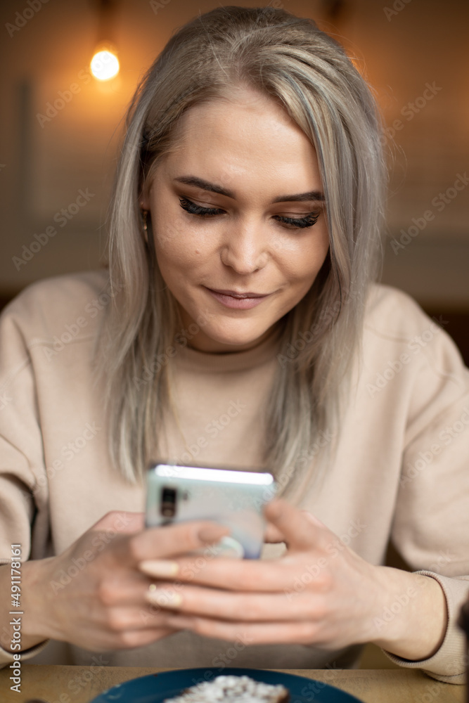 Vertical photo of upset tired woman in beige sweater, with manicure, cafe with plate of food, chatting online. Close up Vertical photo of upset tired woman in beige sweater, with manicure, cafe with plate of food, chatting online. Close up