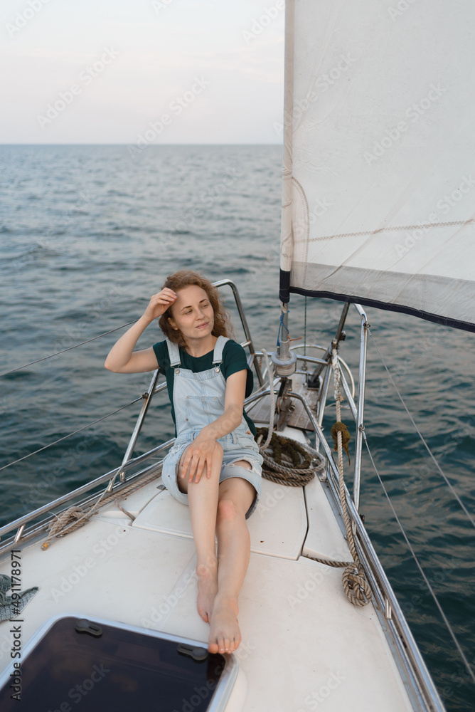A redhead woman is sitting on a yacht and enjoying a trip by the sea