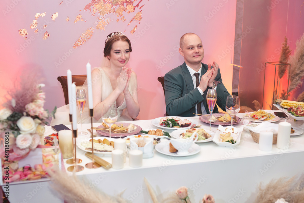 The happy bride and funny groom sit at the table and celebrate the wedding in the banquet hall of the restaurant The happy bride and funny groom sit at the table and celebrate the wedding in the banquet hall of the restaurant