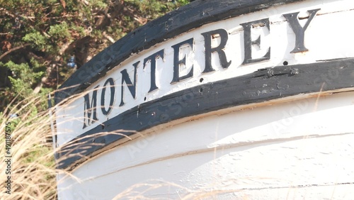 Monterey sign on white wooden boat stern, fisherman nautical vessel stem, bow or rostrum near Cannery Row and Bay Aquarium. Coniferous pine cypress tree. Historic capital, tourist city, California USA photo