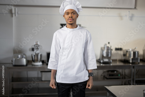 Portrait of handsome latin chef in uniform standing in professional restaurant kitchen. Workers at job concept