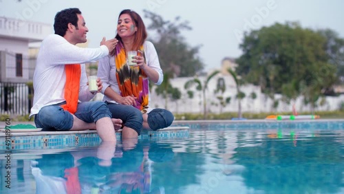 An attractive male in a white Kurta playing Holi with his beautiful wife on a farm - Holi celebrations  organic colors. A young Indian couple having the popular Thandai drink / bhaang while relaxin... photo