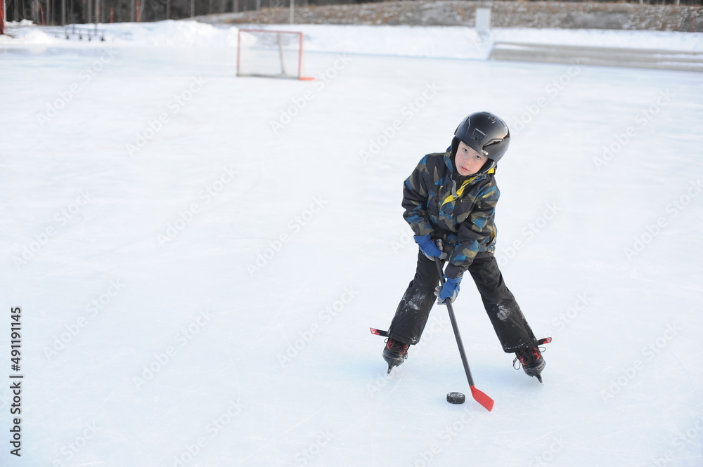 A young boy playing and training ice hockey on outdoor ice rink in winter A young boy playing and training ice hockey on outdoor ice rink in winter