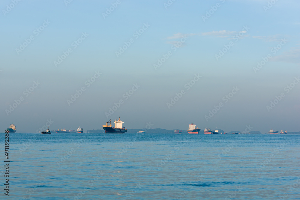 Cargo ships, oil tankers and bulk carriers moored offshore along the Singapore Strait sea, in Singapore, at sunrise. Maritime transport is disrupted following the global supply chain shortage in 2022