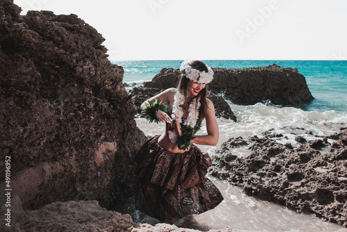 Welcome to hawaii travel summer. Hawaiian hula dancer dancing hawai dance. Young woman smiling with polynesia, tahiti and kauai attire. Bra model with flowers on rocky beach in summer day.