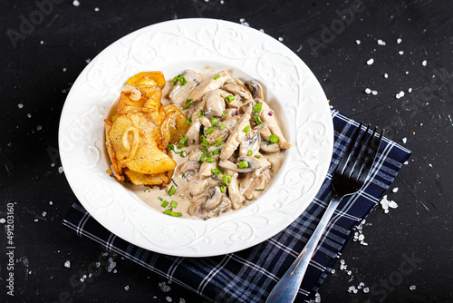 Fotografie on a white plate chicken fricassee with mushrooms, with fried potatoes, on a bla