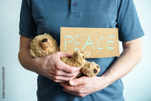Ein Mann hält eine Teddybären und ein Schild mit dem Text Peace in seinen Händen. Frieden, Botschaft.