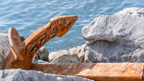 A rusty anchor discarded on a rocky shore