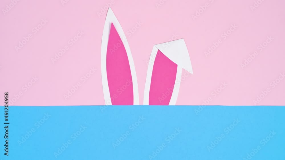 Rabbit ears appear on pastel pink and blue background. Easter copy space stop motion