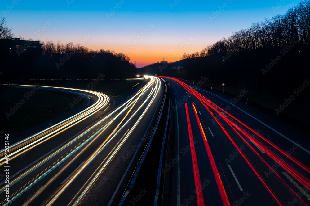 German Autobahn A46 at evening twilight in winter in Iserlohn Sauerland at junction driveway town centre, long time exposure with light traces of passing car lights. Colorful sky gradient after sunset German Autobahn A46 at evening twilight in winter in Iserlohn Sauerland at junction driveway town centre, long time exposure with light traces of passing car lights. Colorful sky gradient after sunset