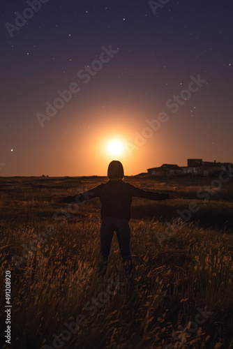 young woman with open arms standing on the field at moon rise
